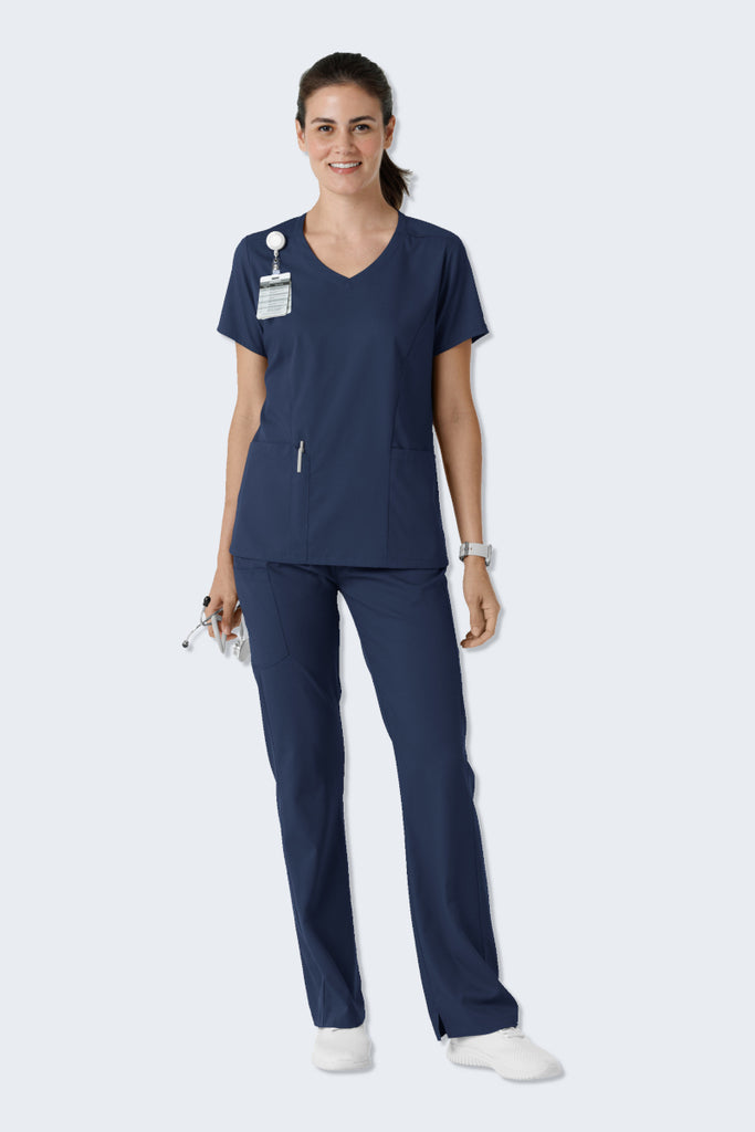 Woman wearing a navy scrub set from WonderWink Boundless, featuring the 6151 Women's V-neck Scrub Top and 5251 Women's Bootcut Scrub Pants. The set combines a modern, professional look with soft, stretchy, and sustainable fabric for comfort throughout the workday. Supplied by Infectious Clothing Co.