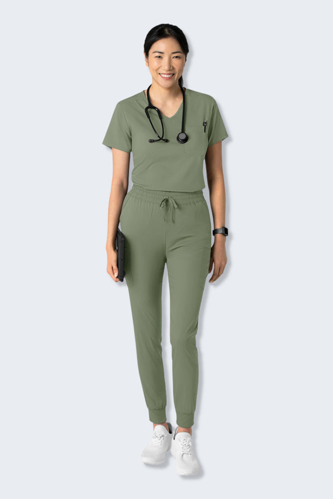 Woman wearing a Sage Green WonderWink Boundless scrub set, featuring the 6151 Women's V-neck Scrub Top and matching jogger pants. The top offers a flattering, modern fit with practical pockets, while the joggers provide comfort with a soft, stretchy, and sustainable fabric. Perfect for healthcare professionals seeking both style and functionality. Supplied by Infectious Clothing Co.