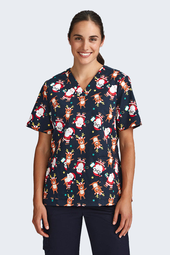 Female model wearing a navy blue Christmas scrub top from Infectious Clothing Company, featuring cute prints of Santa and reindeer. This festive scrub top is perfect for healthcare professionals looking to add holiday spirit to their work attire.