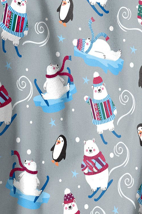 Close-up of a winter-themed Christmas scrub print featuring adorable polar bears in festive sweaters and penguins sledding, set against a light grey background. Available at Infectious Clothing Co. in Australia.